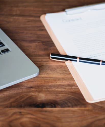 Job contract signing process: laptop, documents, and pen on wooden desk symbolizing candidate onboarding